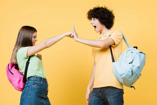 Lächelndes Mädchen mit Rucksack schlägt Handfläche eines aufgeregten Freundes auf gelbem Hintergrund — Stockfoto