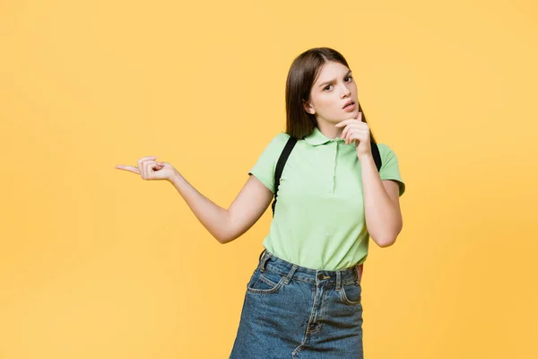 Pensativo adolescente apuntando lejos aislado en amarillo - foto de stock