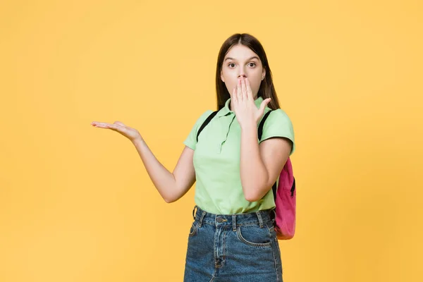 Adolescente asombrado con mochila apuntando con la mano aislada en amarillo - foto de stock