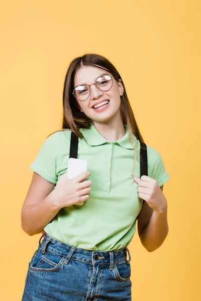 Усміхнений підліток тримає мобільний телефон і рюкзак ізольовано на жовтому — стокове фото