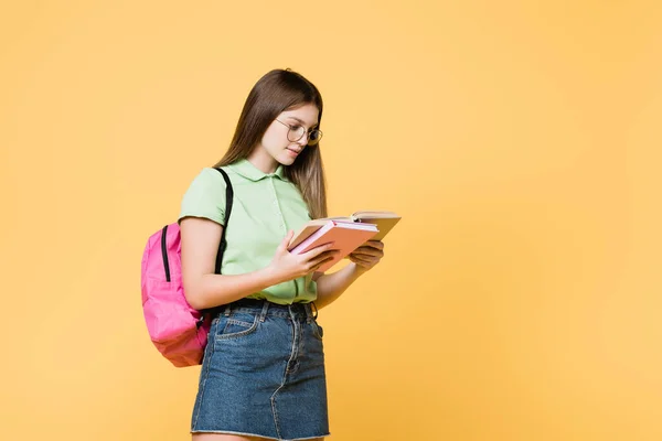 Chica en gafas con mochila libro de lectura aislado en amarillo - foto de stock