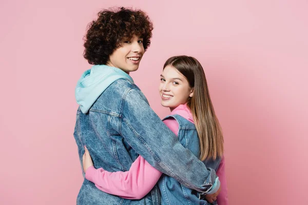 Vue arrière des adolescents souriant à la caméra tout en embrassant isolé sur rose — Photo de stock