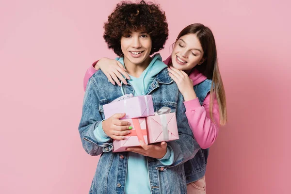 Riccio adolescente in possesso di scatole regalo vicino sorridente ragazza su sfondo rosa — Foto stock