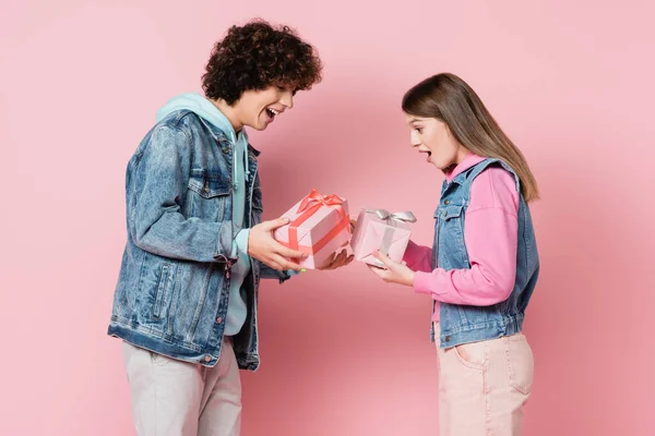 Amazed teen couple looking at gifts on pink background — Stock Photo