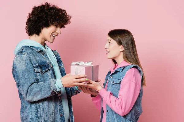 Sonriente pareja adolescente sosteniendo presente con cinta sobre fondo rosa - foto de stock