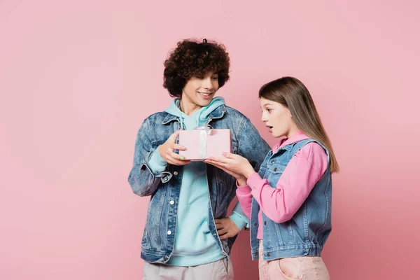 Smiling teenager giving present to excited girlfriend on pink background — Stock Photo