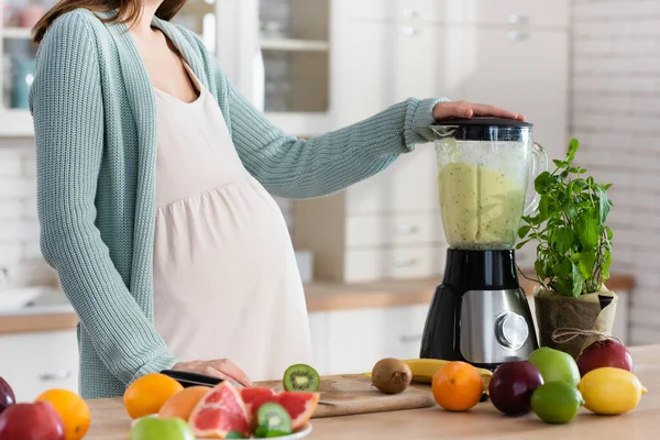 Vista parcial de la mujer embarazada preparando batido de frutas en licuadora — Stock Photo