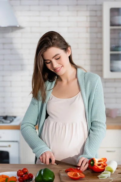 Усміхнена вагітна жінка, що ріже свіжі овочі на сніданок — стокове фото