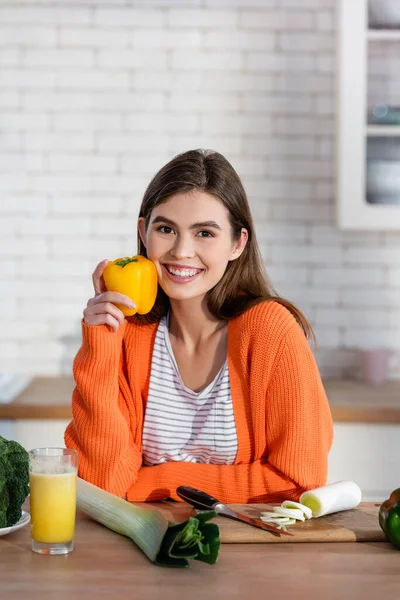Mujer feliz sonriendo a la cámara mientras sostiene el pimiento en la cocina - foto de stock