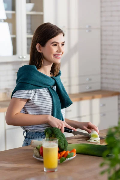 Femme heureuse coupe poireau près du verre de jus frais et légumes sur la table — Photo de stock