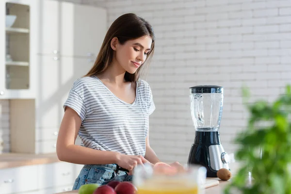 Lächelnde Frau bereitet Frühstück in der Nähe von frischem Obst und Mixer in der Küche zu — Stockfoto