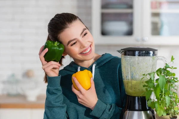Freudige Frau hält Paprika neben Mixer mit Smoothie in Küche — Stockfoto
