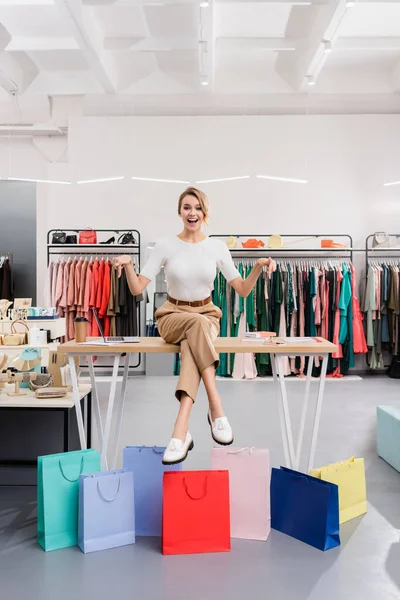 Cheerful seller pointing at shopping bags in showroom — Stock Photo