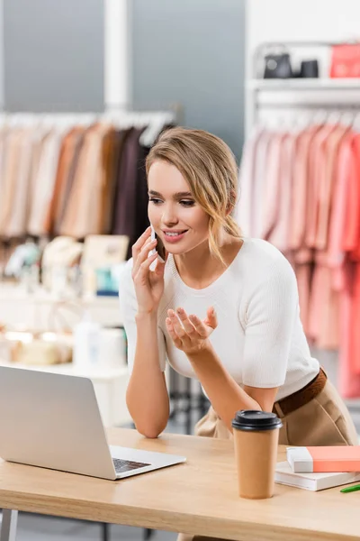 Il giovane venditore accetta l'ordine sul cellulare vicino al laptop e beve da asporto nello showroom — Foto stock