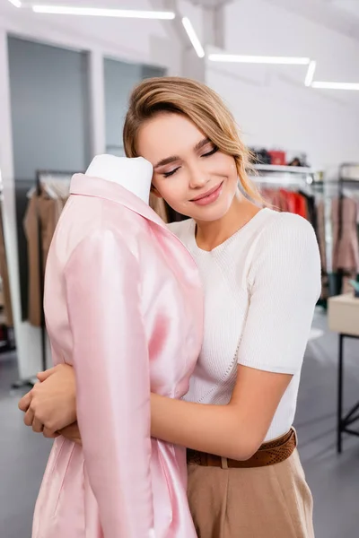 Vendedor sonriente de showroom abrazando abrigo rosa en maniquí - foto de stock