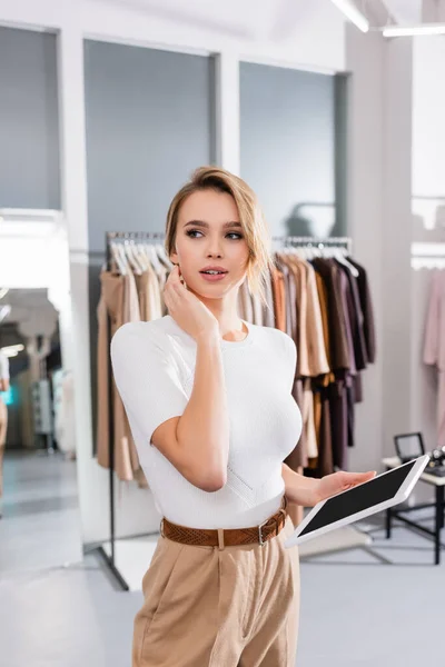 Pretty seller of showroom holding digital tablet and looking away — Stock Photo