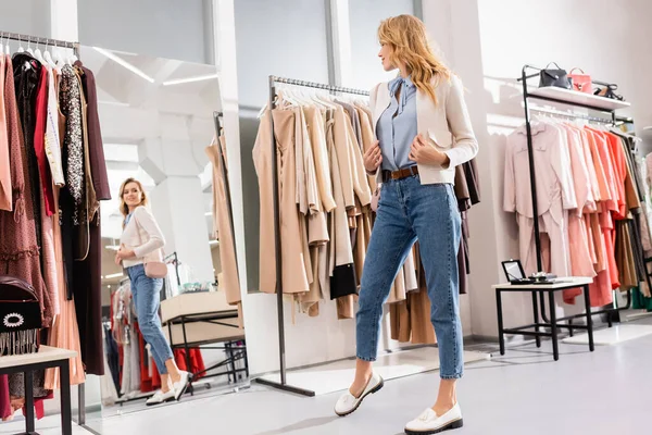 Lächelnde Frau in Jacke blickt im Showroom in den Spiegel — Stockfoto