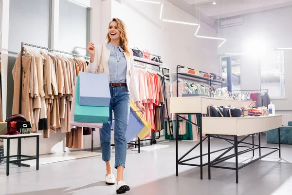 Happy shopaholic walking with shopping bags in showroom — Stock Photo