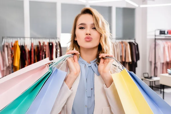 Pretty woman pouting lips while holding shopping bags in showroom — Stock Photo