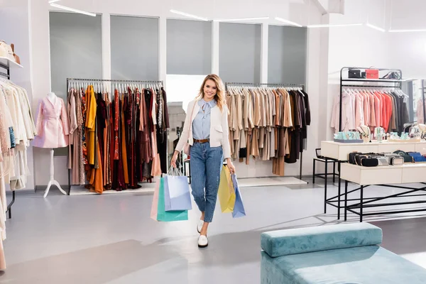 Stylische Frau lächelt, während sie im Showroom Einkaufstüten hält — Stockfoto