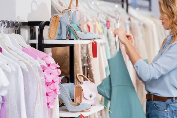 Schuhe und Handtaschen in Regalen neben Kleidung und Frau auf verschwommenem Hintergrund im Showroom — Stockfoto