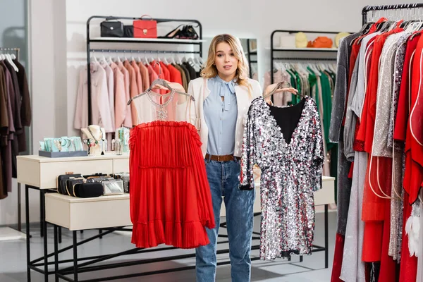 Blonde woman holding hangers with dresses in showroom — Stock Photo