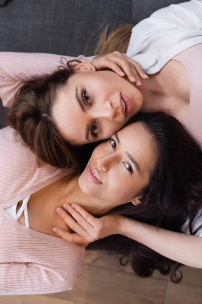 Vista superior de lesbianas positivas abrazándose en la sala de estar - foto de stock
