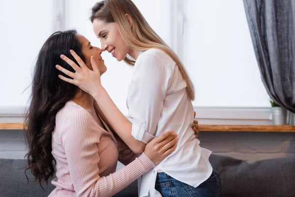 Seitenansicht von lächelnden Freundinnen, die sich im Wohnzimmer umarmen — Stockfoto