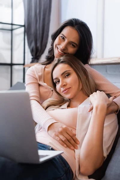 Happy lesbian couple watching movie on laptop and hugging at home - foto de stock