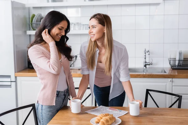 Happy woman looking at shy girlfriend in kitchen — Fotografia de Stock