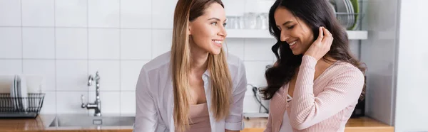 Happy woman looking at shy girlfriend in kitchen at home, banner — Stock Photo