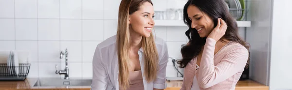 Happy woman looking at shy girlfriend in kitchen at home, banner — Fotografia de Stock