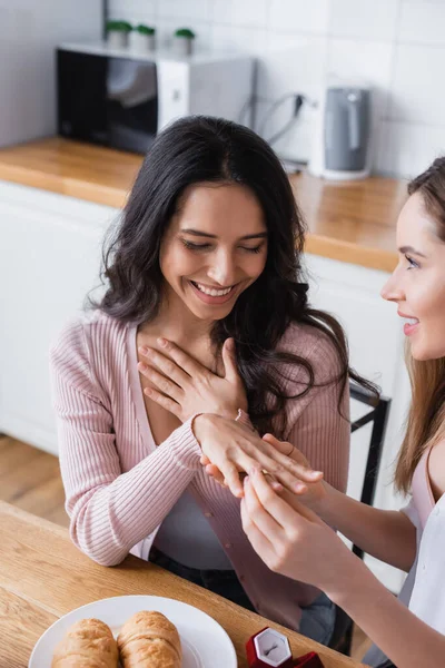 Happy woman wearing wedding ring on finger of cheerful girlfriend at home — Stock Photo