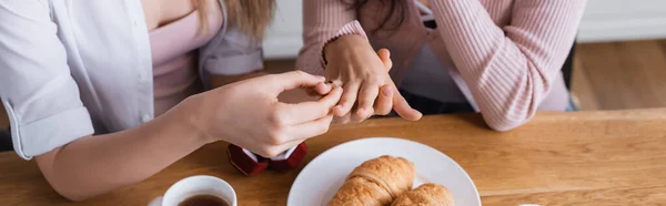 Cropped view of woman wearing wedding ring on finger of girlfriend at home, banner - foto de stock