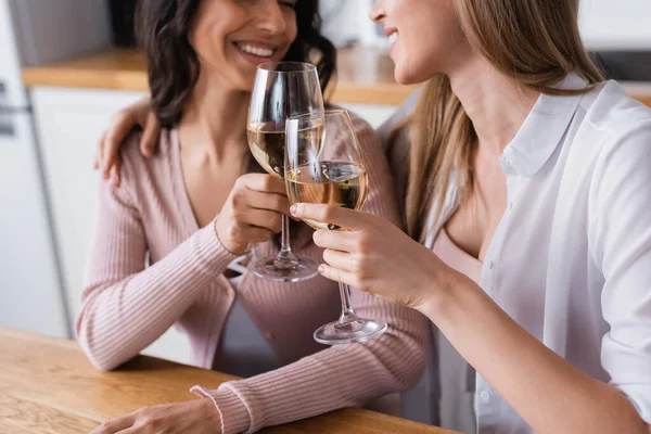 Cropped view of happy lesbian couple clinking glasses of white wine in kitchen — Photo de stock