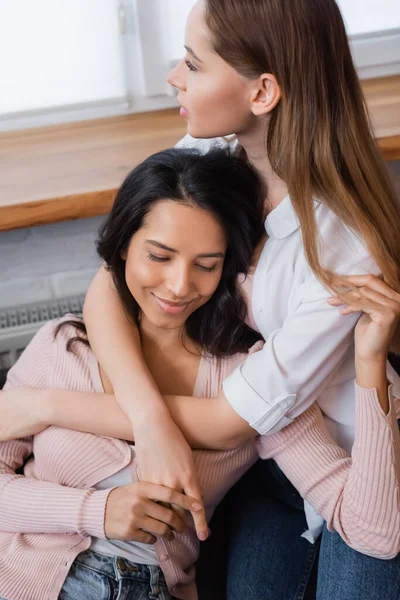 Happy lesbian woman embracing girlfriend in living room - foto de stock