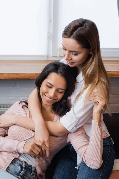 Lächelnde lesbische Frau umarmt Freundin im Wohnzimmer — Stockfoto