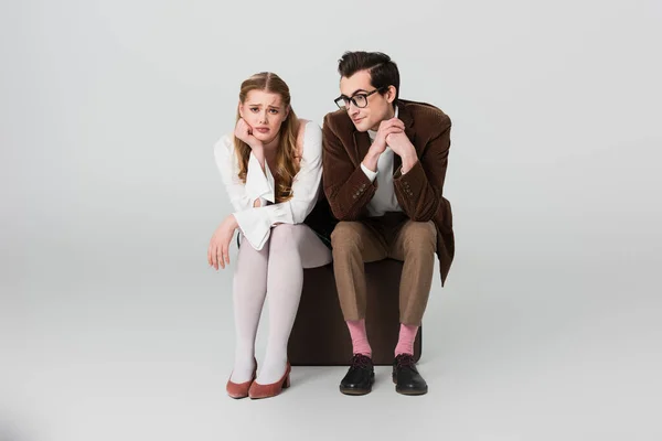 Upset couple in vintage outfit sitting on suitcase on grey background — Stock Photo