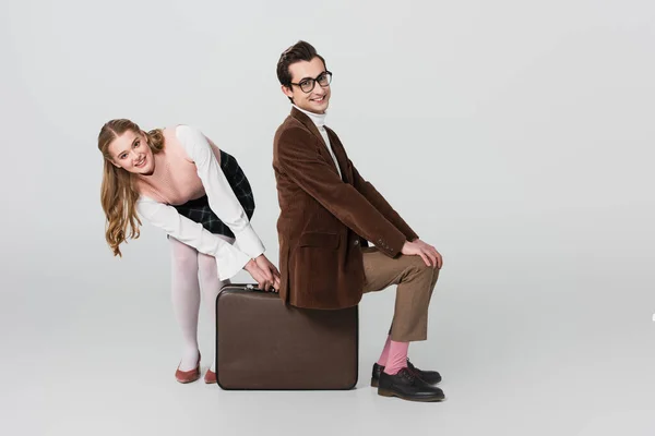 Cheerful woman taking away suitcase from under smiling boyfriend on grey background — Stock Photo