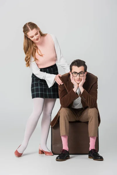 Smiling woman touching shoulder of man sitting on suitcase on grey background — Stock Photo