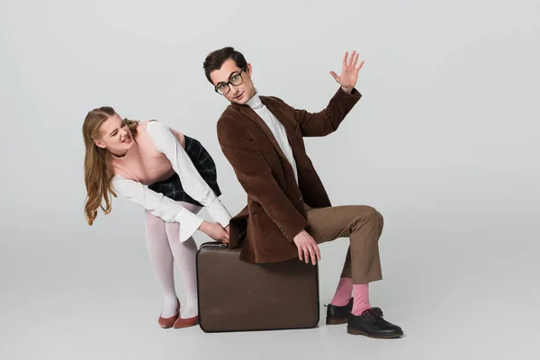 Excited woman taking away vintage suitcase from under boyfriend on grey background — Stock Photo