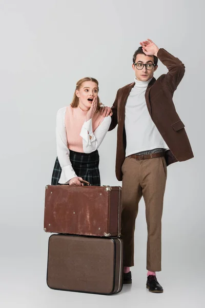 Chocado estilo retro casal olhando para longe perto de malas em fundo cinza — Fotografia de Stock