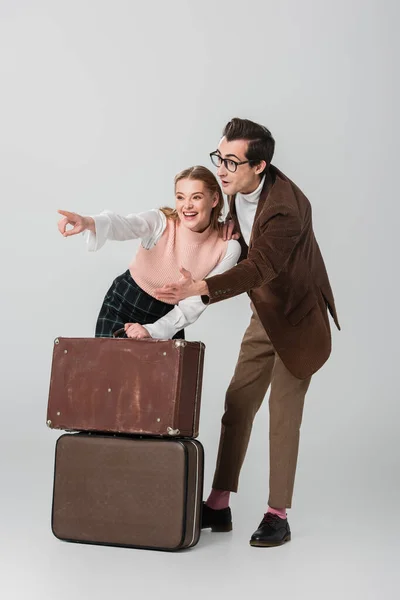 Изумленная пара смотрит в сторону винтажных чемоданов на сером фоне — стоковое фото