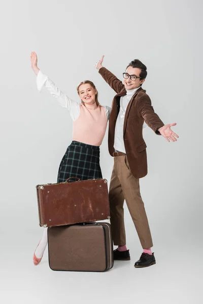 Alegre pareja de pie con los brazos abiertos cerca de las maletas vintage sobre fondo gris - foto de stock