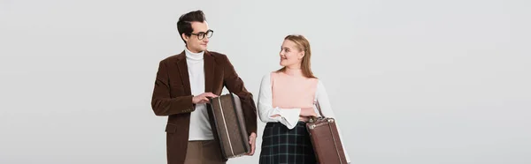 Glückliches Paar im Vintage-Outfit, das sich anschaut, während es Koffer isoliert auf grauem Banner hält — Stockfoto