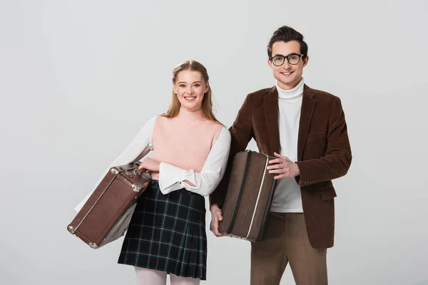 Retro style couple smiling at camera while holding vintage suitcases isolated on grey — Stock Photo