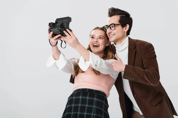 Excited woman with vintage camera taking selfie with man showing thumb up isolated on grey — Stock Photo