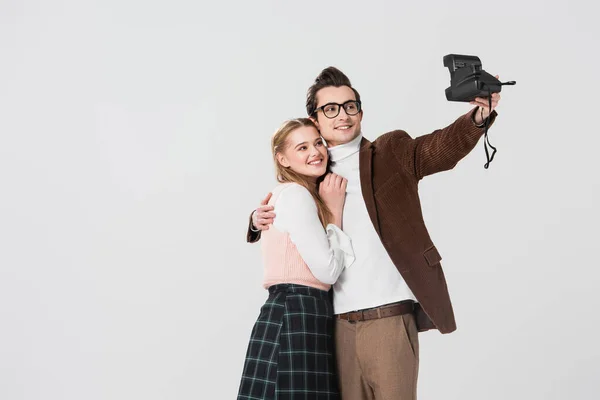 Happy man hugging girlfriend while taking selfie on vintage camera isolated on grey — Stock Photo