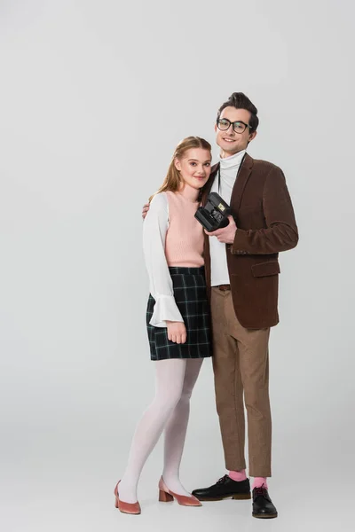 Full length view of happy man with vintage camera embracing girlfriend on grey — Stock Photo