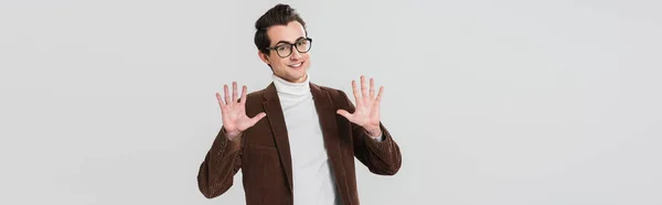 Cheerful man in eyeglasses and brown blazer posing with open palms isolated on grey, banner — Stock Photo